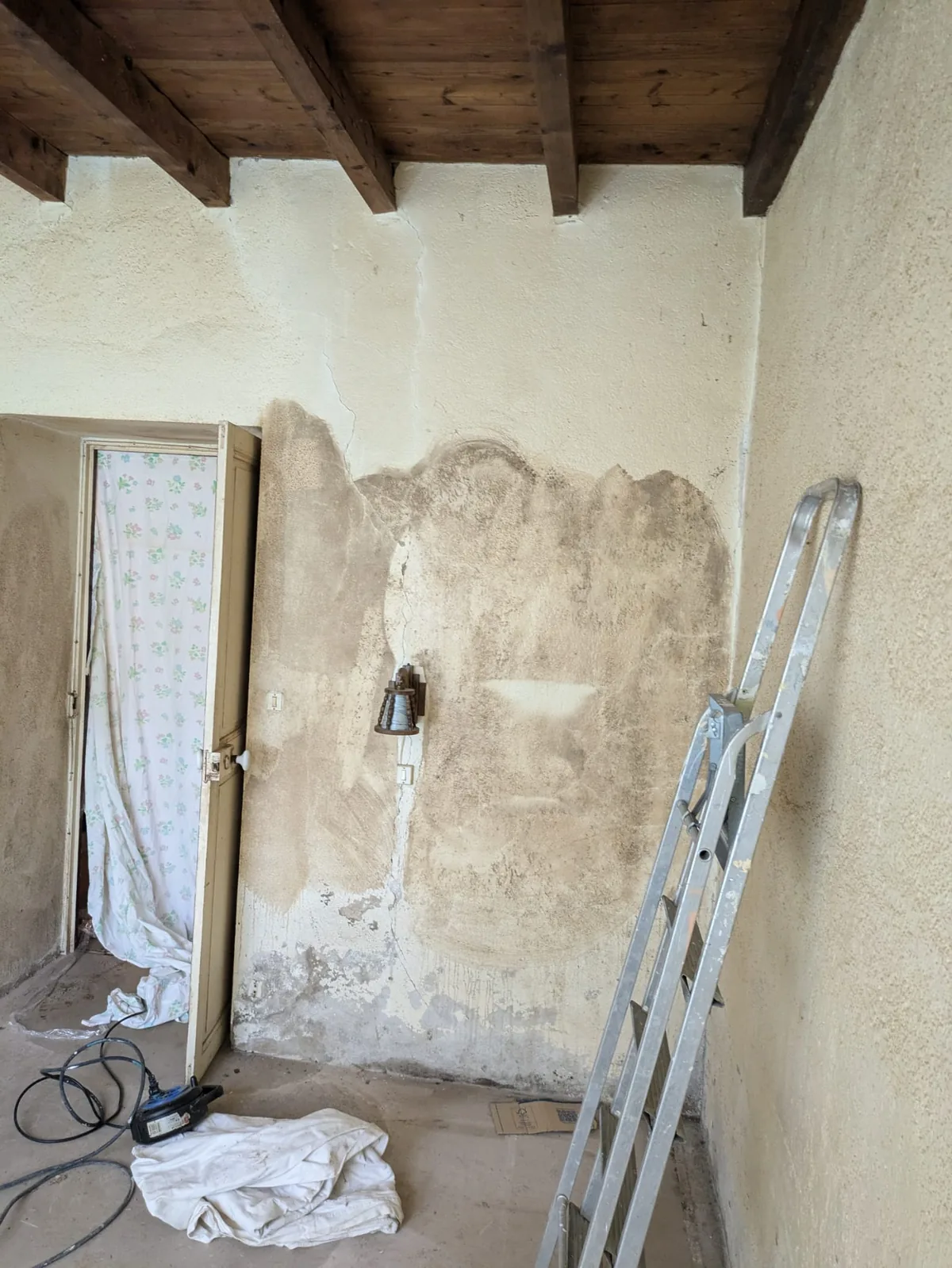 La chambre avant travaux : mur ancien décapé, taches d'humidité et fissures apparentes, échelle posée contre le mur, plafond à poutres apparentes
