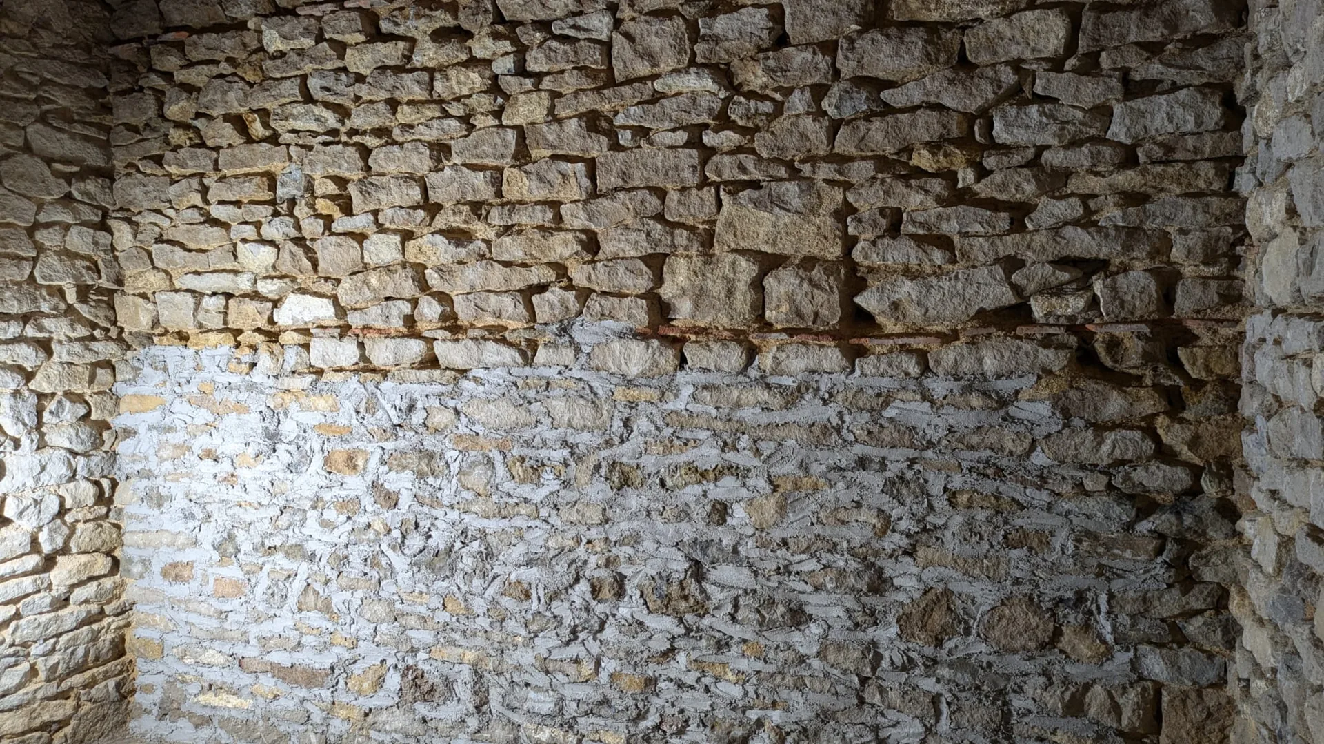 Mur intérieur en pierre dont la moitié basse vient d'être rejointoyée à la chaux, encore claire, la moitié haute restant à nu
