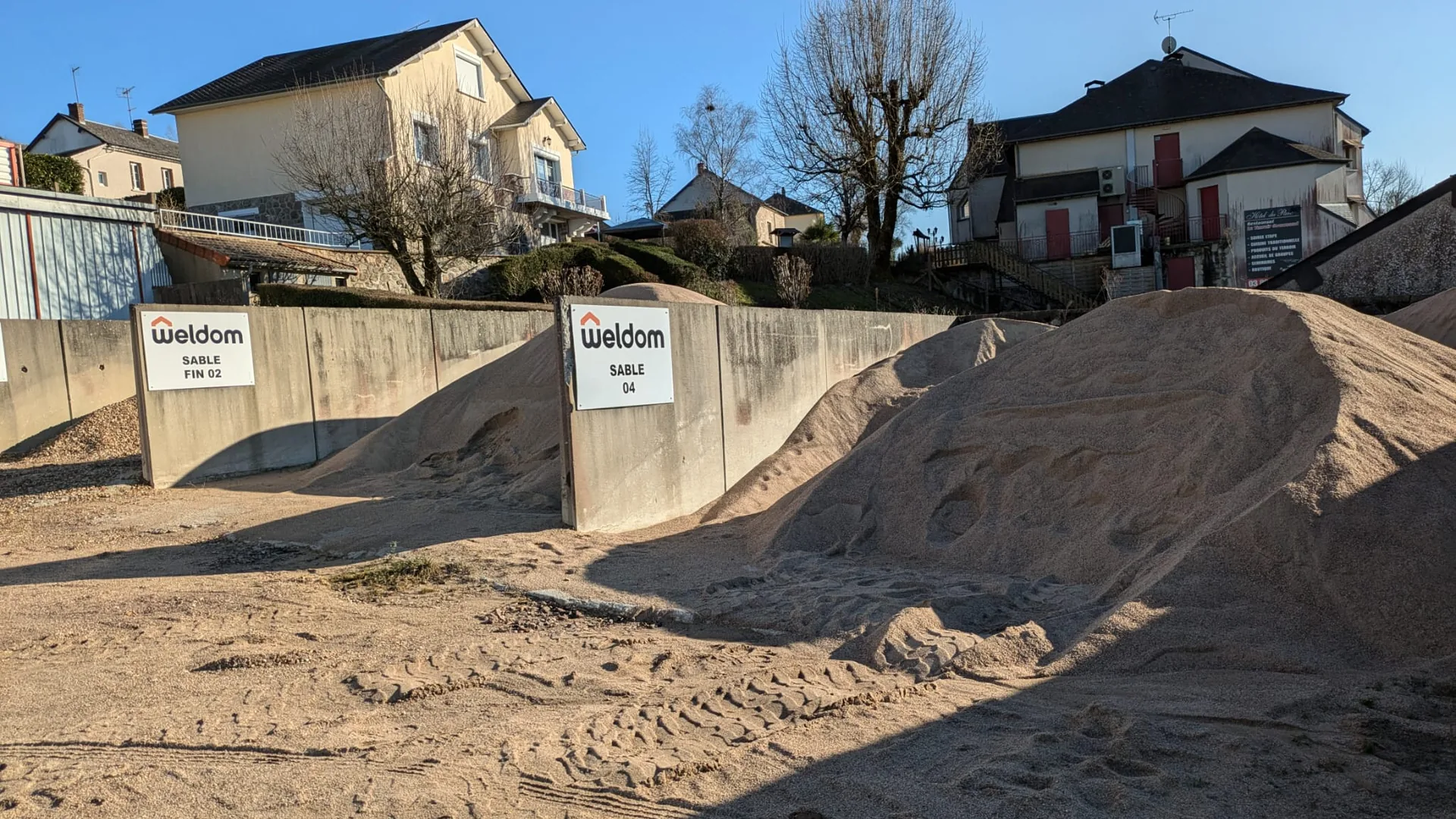 Deux tas de sable séparés chez un négociant de matériaux, signalés par des panneaux « SABLE FIN 02 » et « SABLE 04 »