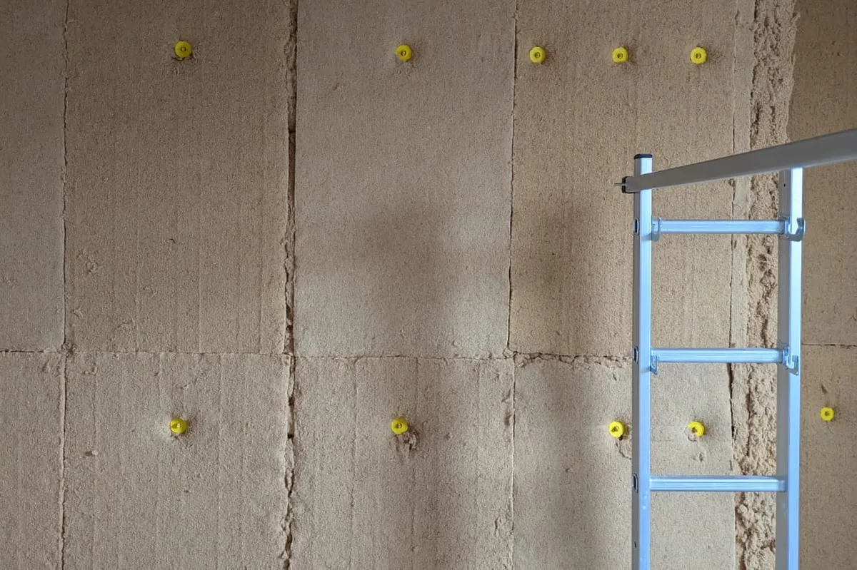 Panneaux de fibre de bois posés sur un mur ancien, fixés par rosaces, sur un chantier d'isolation intérieure