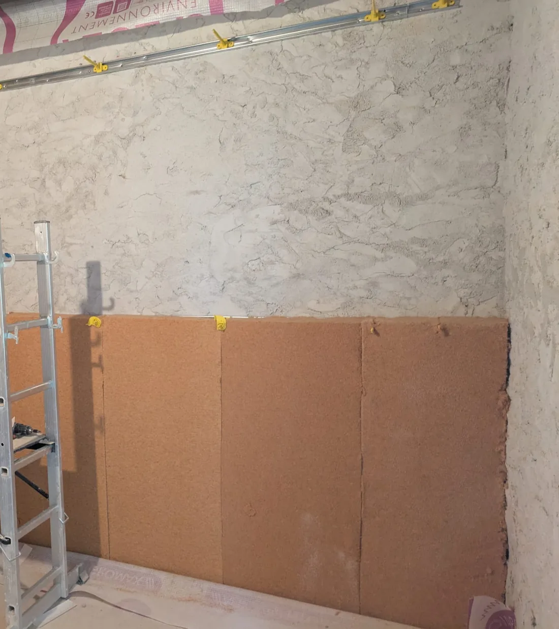 Panneaux de fibre de bois posés contre un mur ancien en pierre enduit à la chaux, sur un chantier d'isolation intérieure