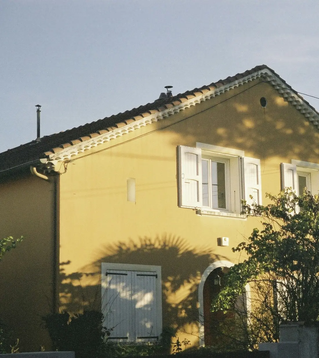 Façade d'une maison individuelle en crépi clair avec ses volets, en fin de journée